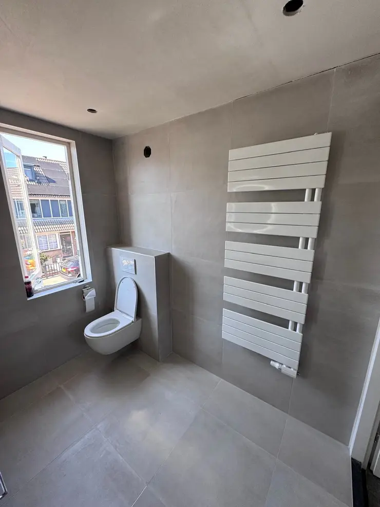 Een hoge witte designradiator op een pas getegelde badkamerwand